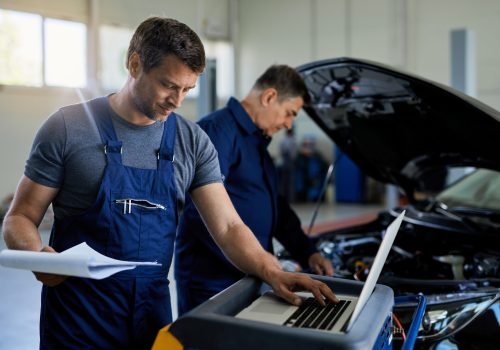 Mid adult mechanic working on laptop while running car diagnostic with his coworker in auto repair shop.